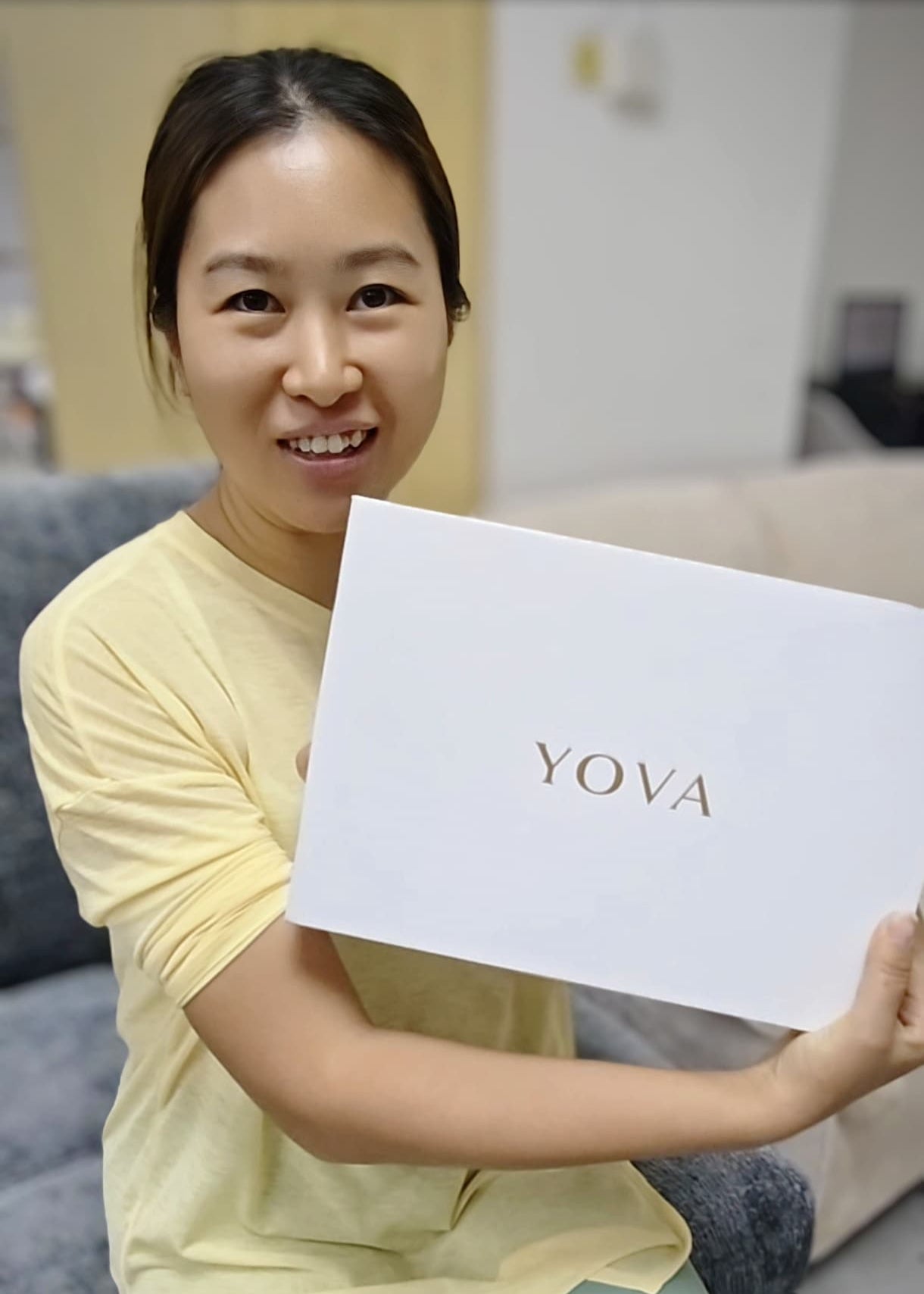 Woman holding a white box with 'Yova' branding in an indoor setting.